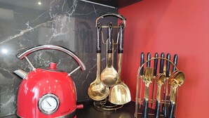 Een rode waterkoker, een set gouden keukengerei en een lepelenhouder op een zwart aanrecht tegen een rode muur.