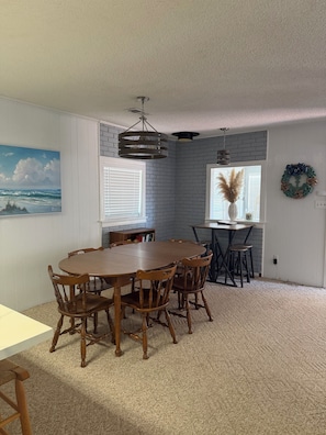 A dining area with a wooden table and chairs, a hanging light fixture, and a view of the outdoors through a window.