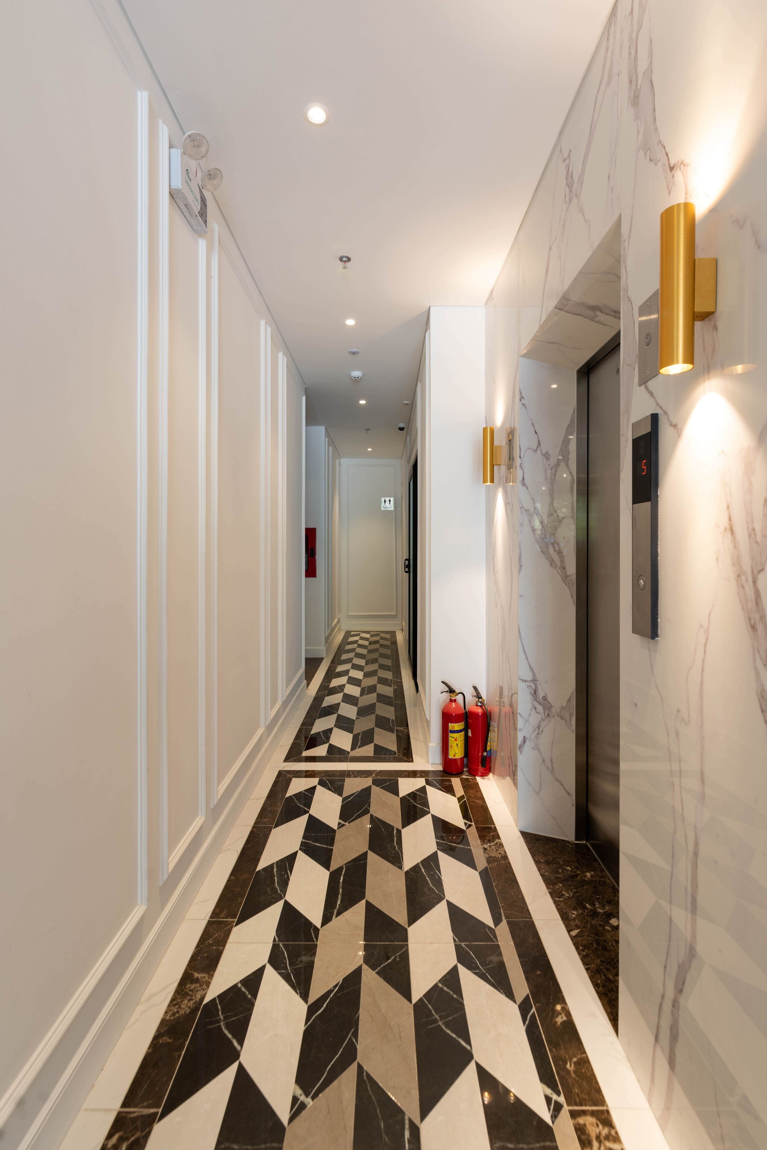 A hallway with a checkered floor, marble walls, and a fire extinguisher.