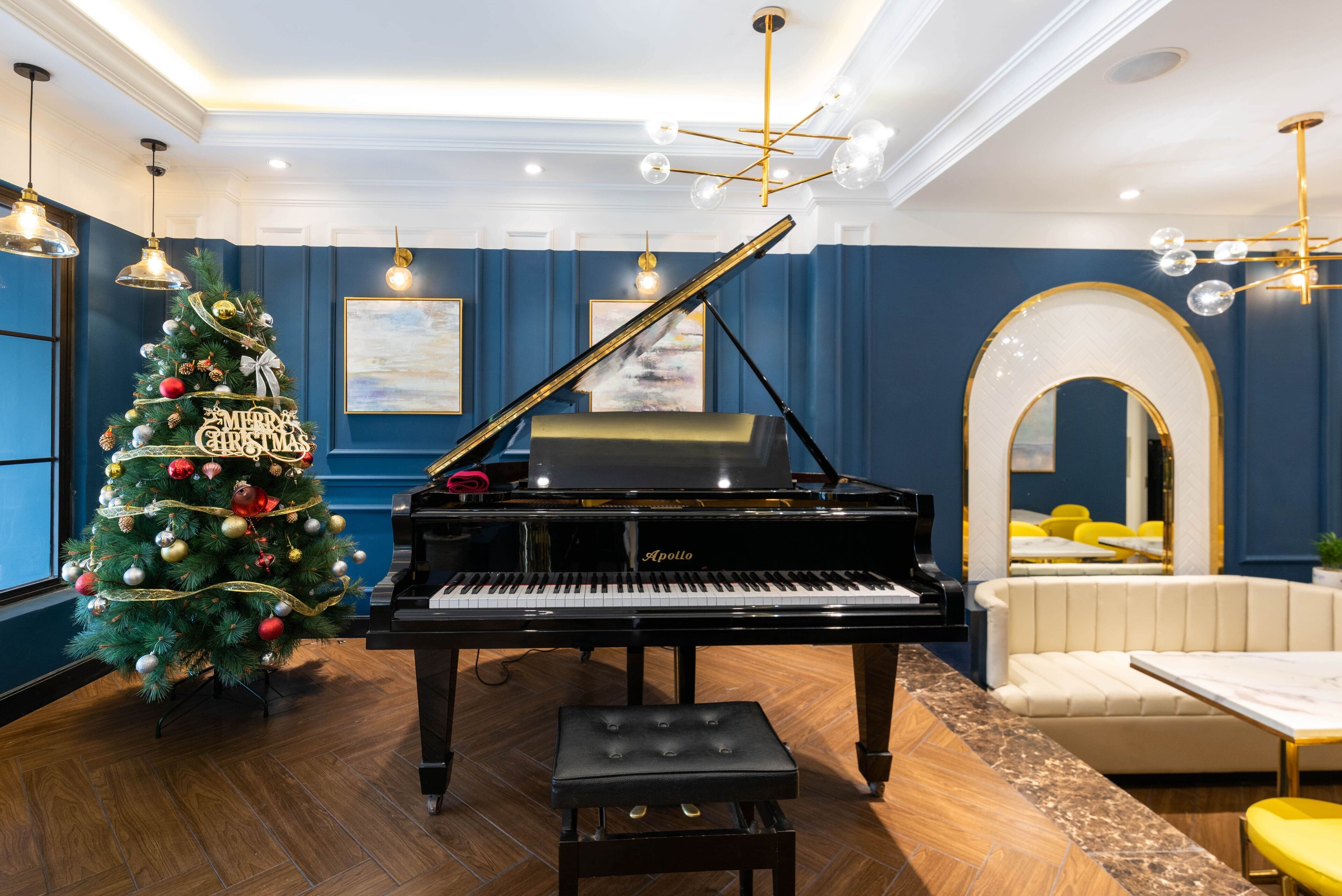 Un piano de cola en una habitación con paredes azules, un árbol de Navidad y un sofá blanco.