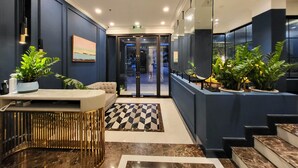 Um lobby de hotel moderno com balcão de recepção, área de estar e uma escadaria.