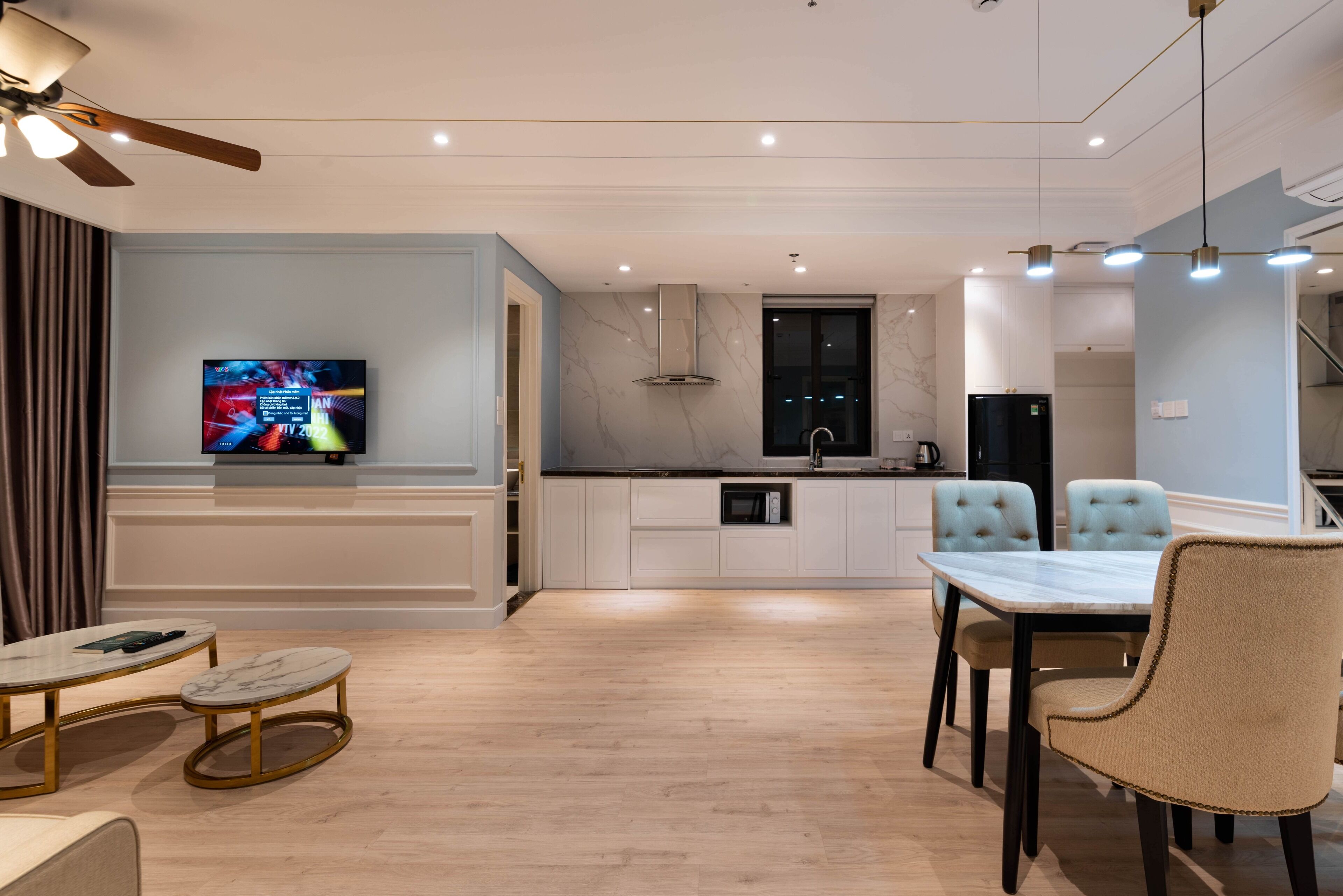A modern kitchen with white cabinets, a marble backsplash, and a black refrigerator. There is a dining area with a table and chairs, and a ceiling fan above.