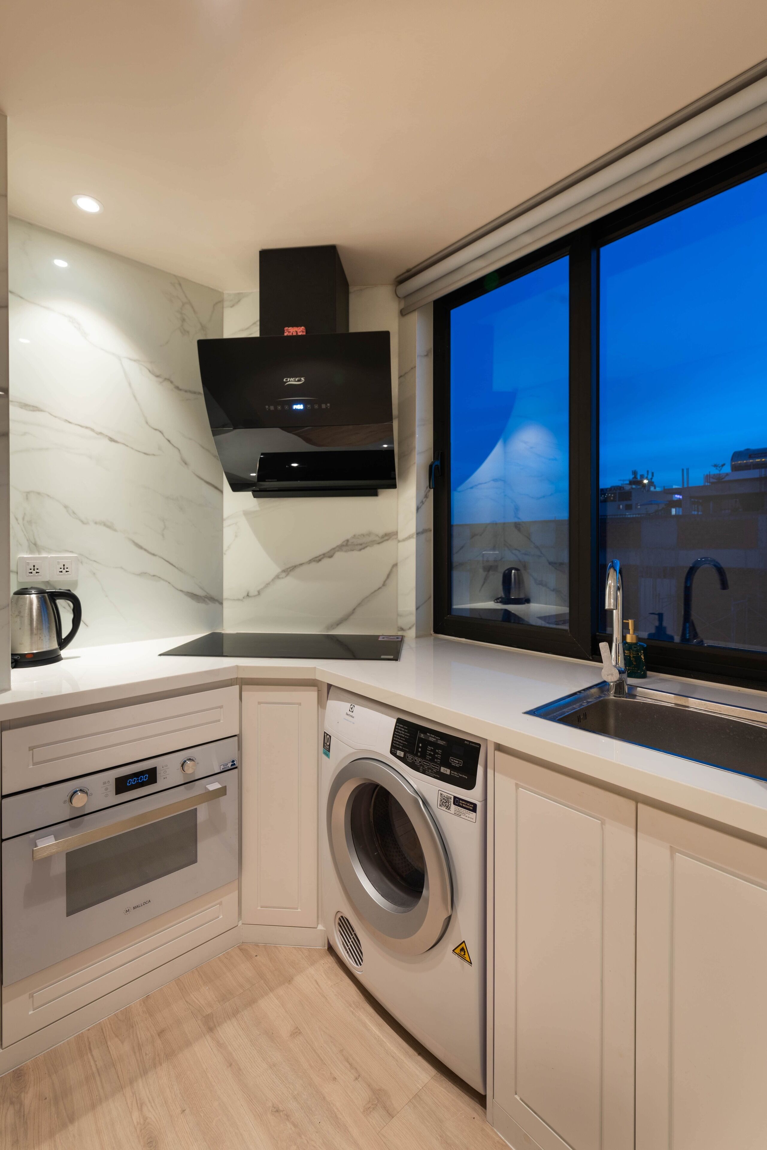 A modern kitchen with a built-in washing machine, a coffee maker, and a window with a city view.