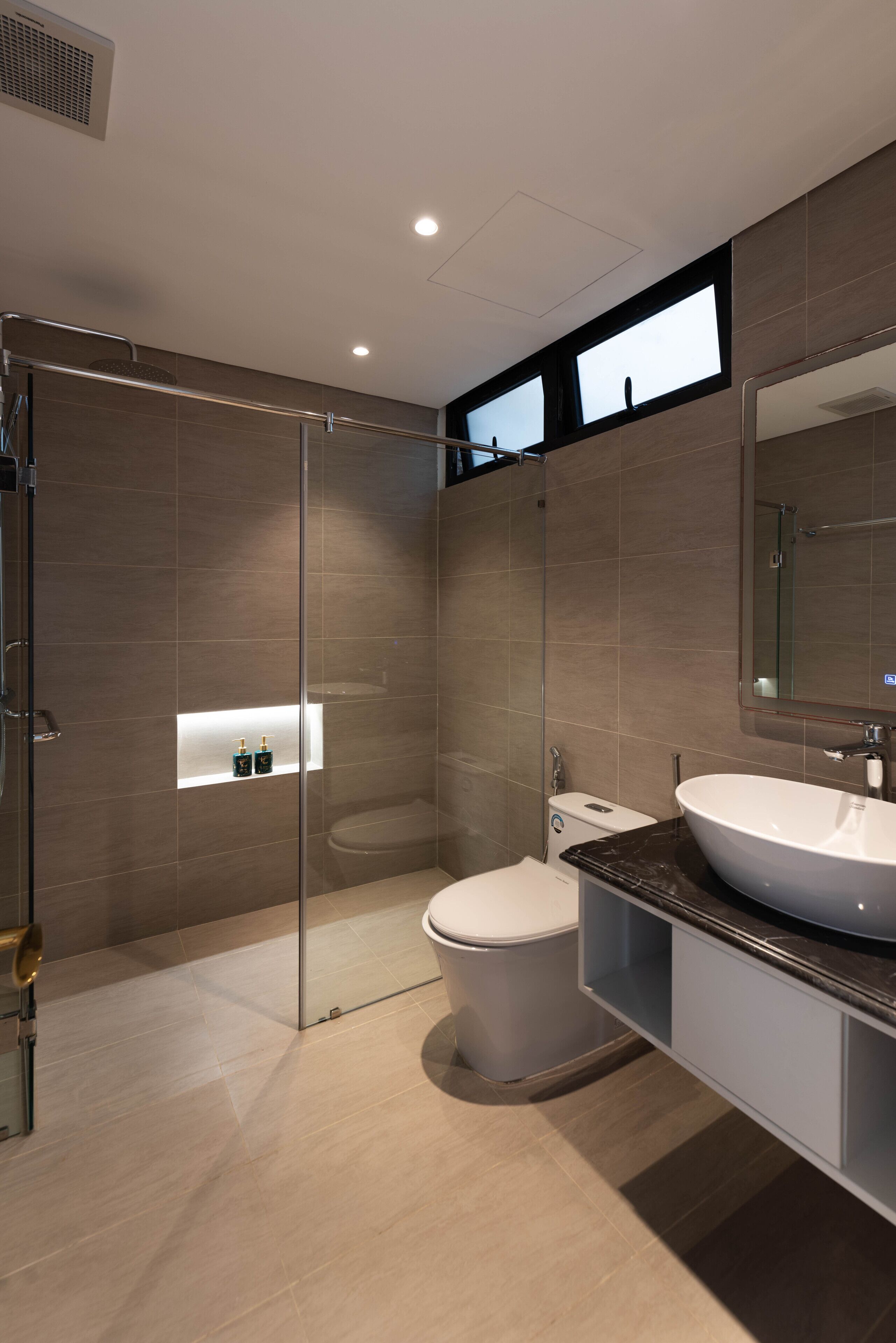 Et moderne badeværelse med et glasafskærmet brusebad, toilet og et vaskeskab med et stort spejl.