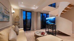 Uma sala de estar moderna com sofá, uma mesa de centro com maçãs, televisão e vista da cidade ao entardecer.