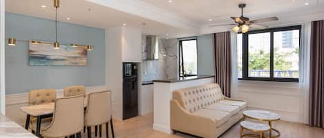 A modern living room with a sofa, dining table, chairs, and a kitchen area with a refrigerator.