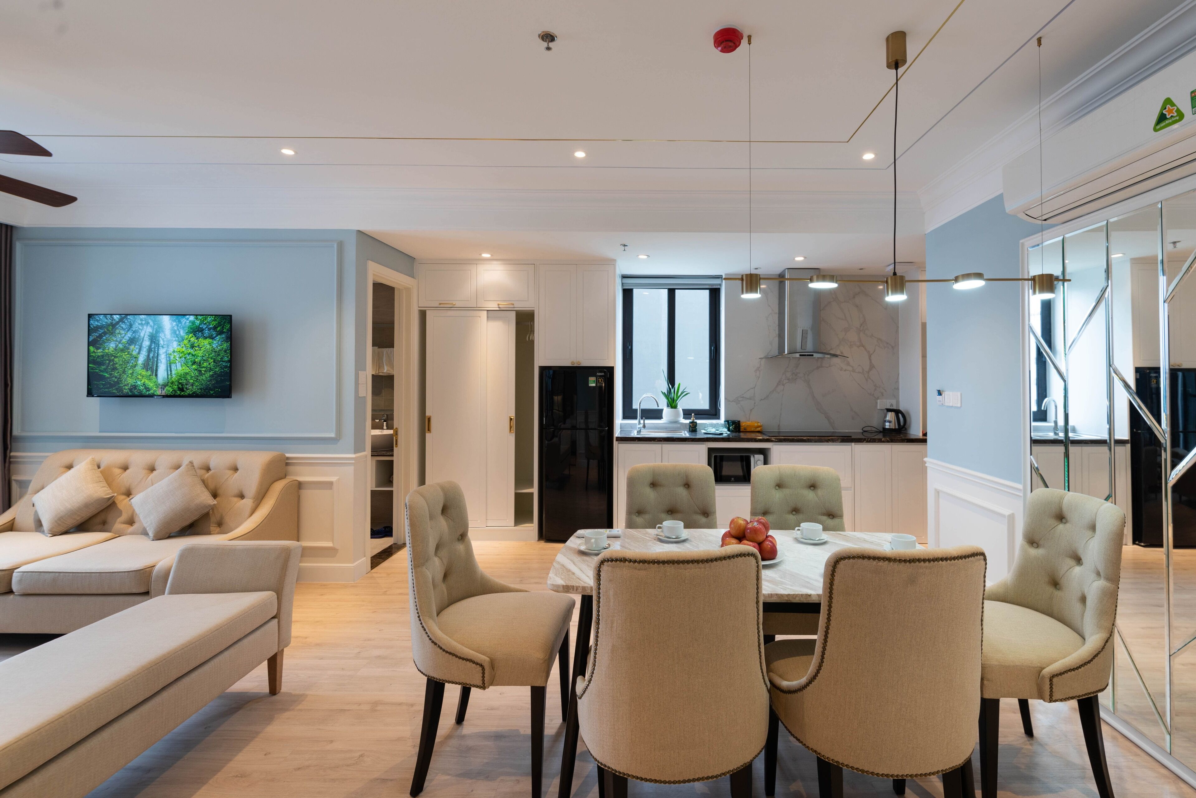 A modern living room with a sofa, dining area with chairs, a TV, and a kitchen in the background.