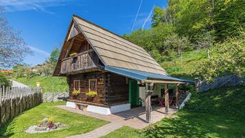 Une cabane en bois avec un toit en pente, une véranda et un petit jardin agrémenté de fleurs et d’un élément décoratif en pierre.
