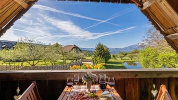 Une table en bois, sur laquelle sont disposés un plateau de fromages, des verres à vin et une carafe, le tout placé devant un paysage montagneux pittoresque.