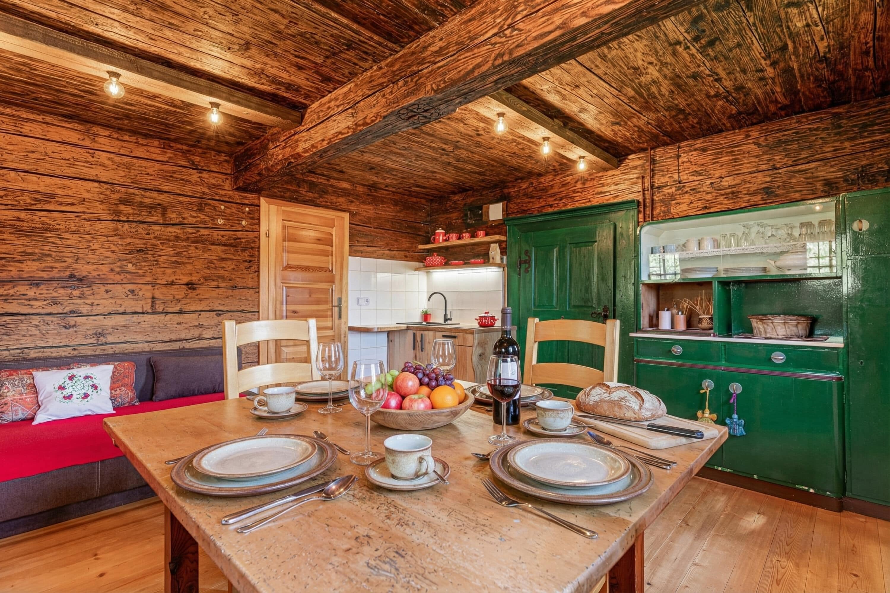 Un intérieur en bois avec une table à manger pour quatre personnes, un coin cuisine et un canapé rouge.