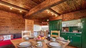 A wooden interior with a dining table set for four, a kitchen area, and a red sofa.
