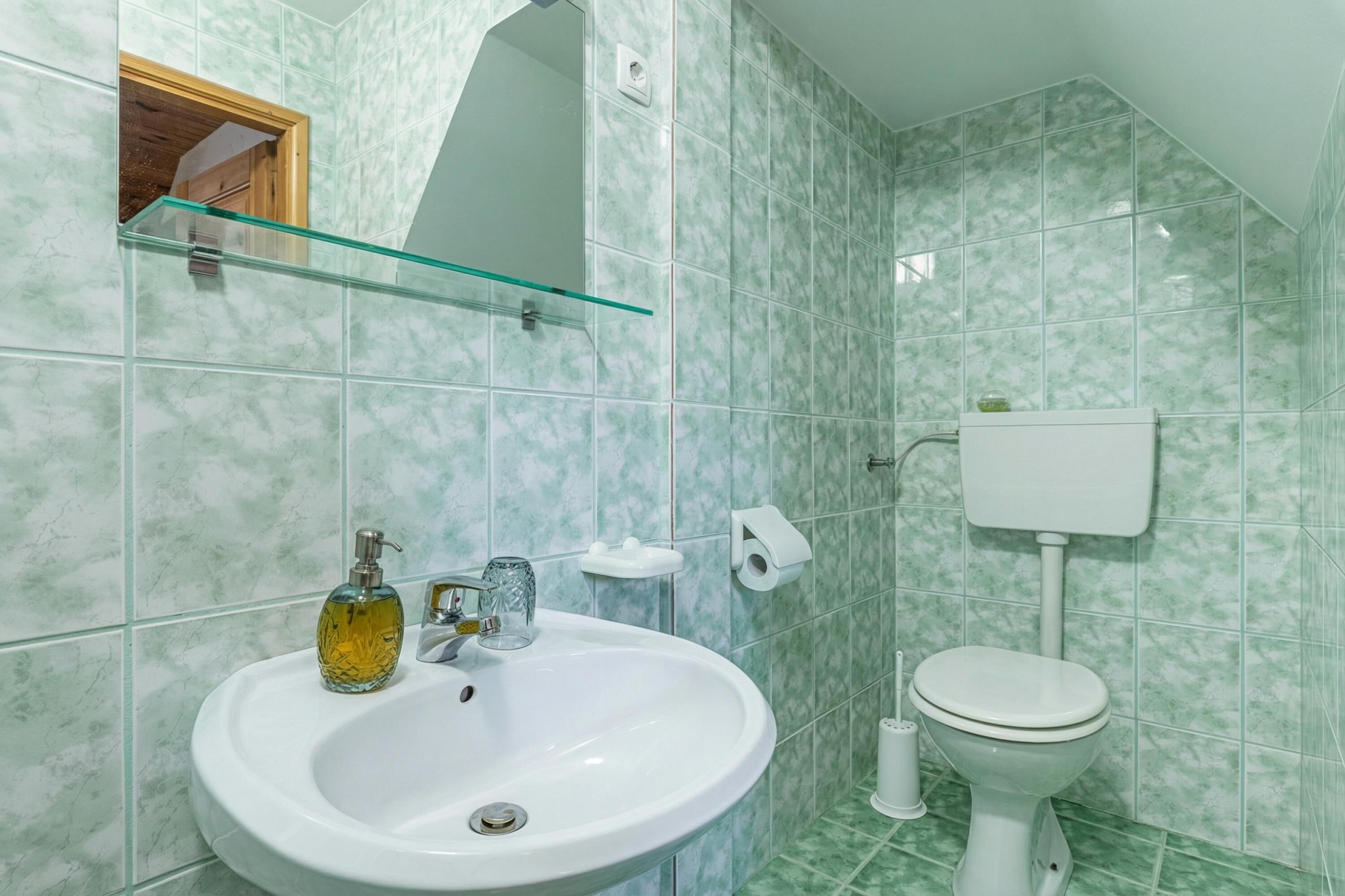 A bathroom with a white sink, glass soap dispenser, and a toilet.