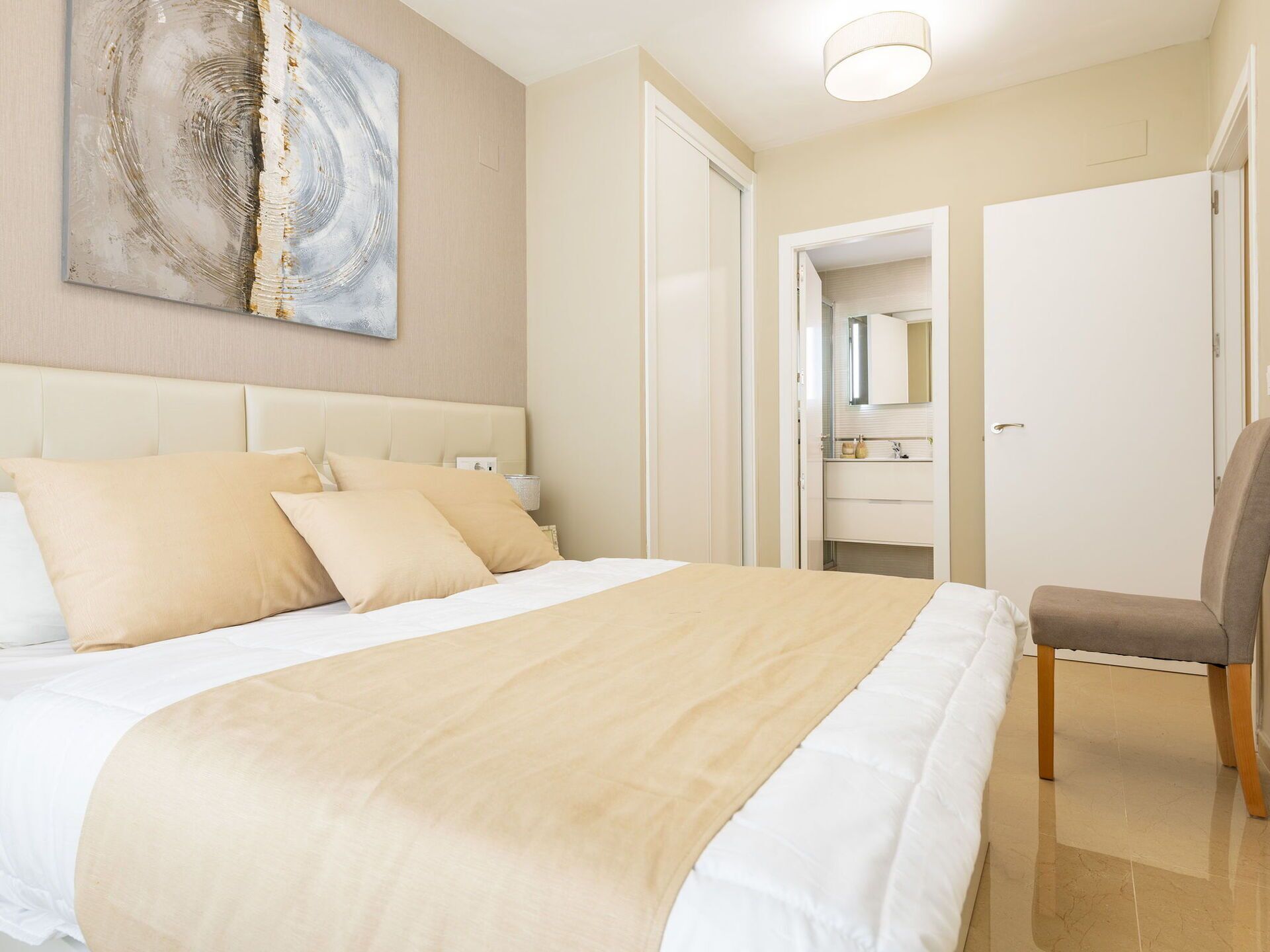 Une chambre d’hôtel avec un grand lit, une chaise, une salle de bain avec un miroir et un tableau au mur.