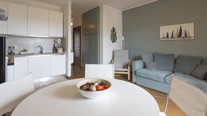 Et moderne køkken med hvide skabe, et spisebord med mad i en skål, en grå sofa og en kaktus på væggen.