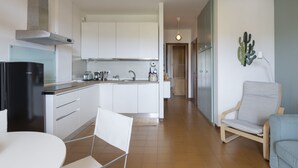 Et moderne køkken med lyse skabe, et sort køleskab og et spiseområde med et hvidt bord og en stol.