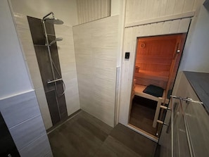 A compact bathroom with a shower, a wooden sauna, and a small seating area. - Holiday Home Sailorskoje (Kappeln)