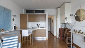 Een moderne keuken met houten kastjes, een wit aanrecht en een roestvrijstalen spoelbak. Er is een eethoek met gestreepte stoelen en een tafel.