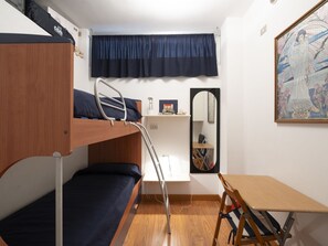 Une chambre de dortoir avec des lits superposés, un bureau, une chaise, un miroir et un tableau accroché au mur.