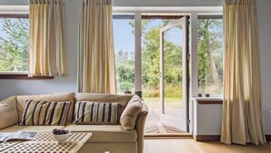 A cozy living room with a sofa, a table with a bowl of fruit, and a view of a garden through large sliding glass doors. - Cozy home in Græsted with sauna (Græsted)