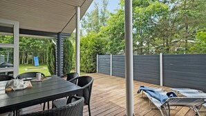 Un espace extérieur aménagé en terrasse avec une table et des chaises, un coin salon couvert et une vue sur une aire de jeux et des arbres.