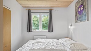 Une chambre à coucher avec un lit, une fenêtre avec des rideaux, une lampe de chevet et un tableau au mur.