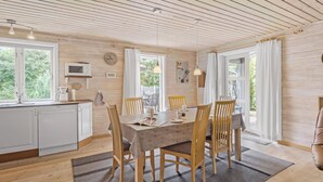 Un intérieur en bois comprenant une table à manger, des chaises, un coin cuisine et de grandes fenêtres.