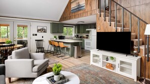 A modern living room with a sofa, TV, and a small coffee table. - Cozy chalet w/ forest views & hot tub (Hedgesville)
