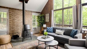 A cozy living room with a fireplace, a sofa, and a large window overlooking a forest. - Cozy chalet w/ forest views & hot tub (Hedgesville)