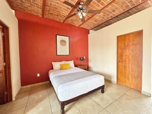 Ein Schlafzimmer mit einem Bett, einem Deckenventilator, einer Holztür und einer roten Wand.