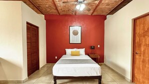 A bedroom with a bed, a ceiling fan, a red wall, and a wooden door. - Tranquil Studio Suite with Outdoor Salt Water Pool (Ajijic)