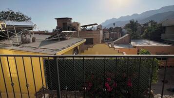 A rooftop with a metal fence, a yellow structure, and a view of distant mountains.