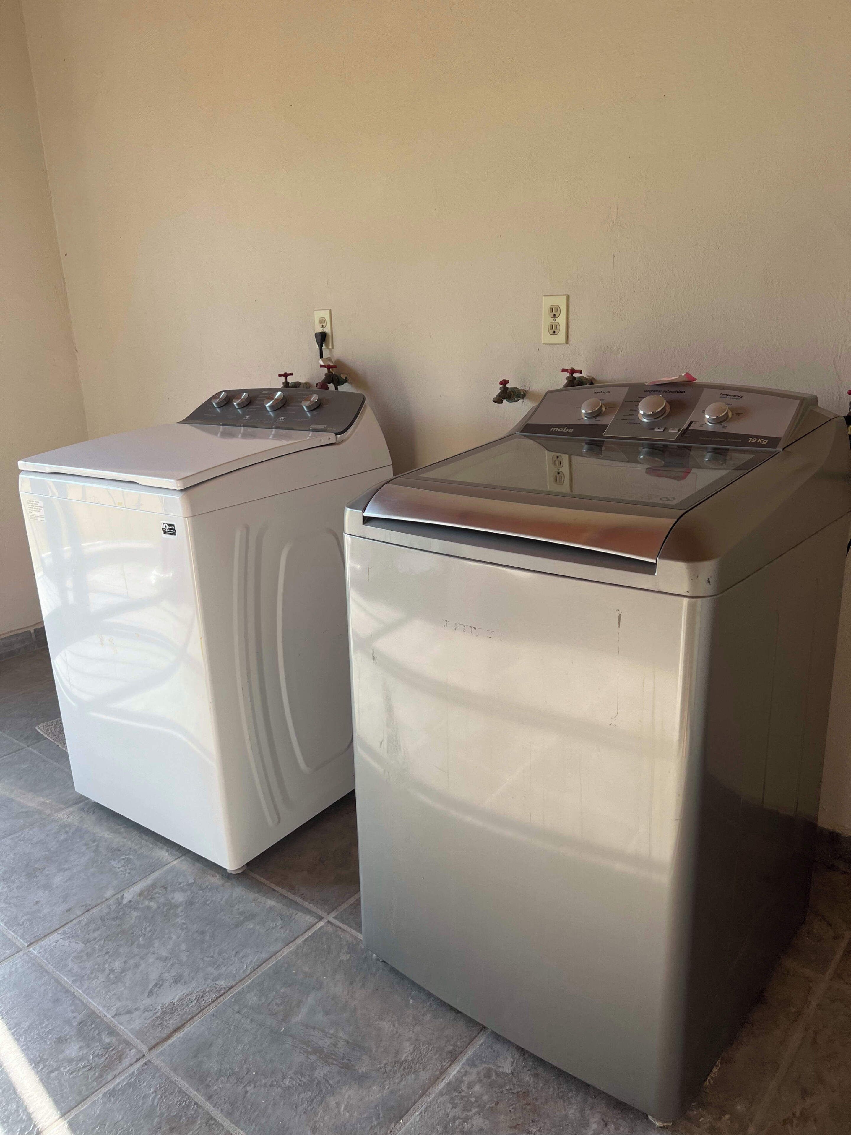 Two stacked washing machines in a room with tiled flooring and a plain wall.