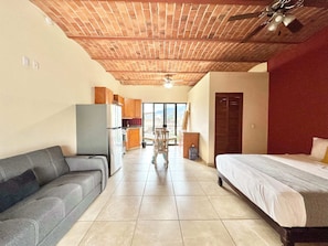 A room with a bed, a sofa, a kitchenette, and a view through a glass door. - Tranquil Studio Suite with Outdoor Salt Water Pool (Ajijic)