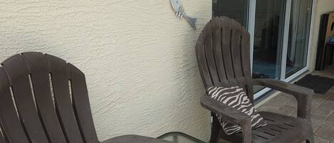 Two plastic chairs with armrests and a glass table on a patio with a textured wall and decorative fish and dragonfly art.