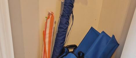 A corner of a room with a tiled floor, a white door, and a wall. There are several bags and umbrellas stacked against the wall.
