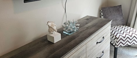Una habitación con un televisor de pantalla plana montado en la pared, un aparador de madera con cajones, una concha decorativa y un coral sobre el aparador.