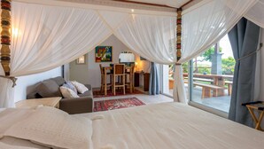 Un dormitorio amplio con una cama grande, una zona de estar con una mesa y sillas, y vistas al patio exterior.