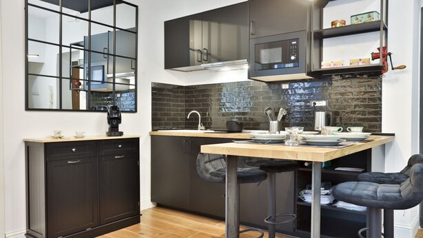 Una cocina moderna con armarios oscuros, microondas, cafetera y un taburete de bar.