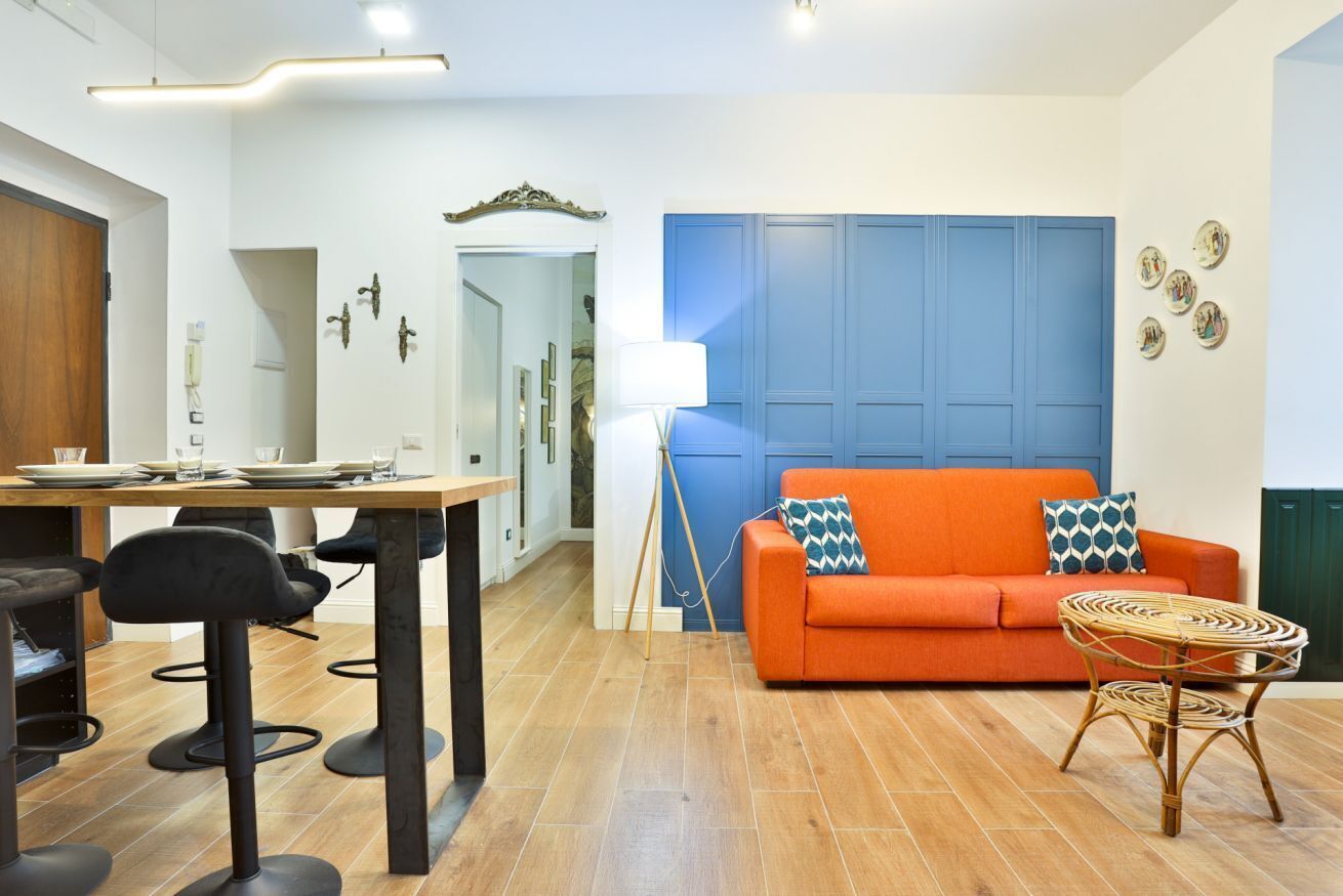 Een moderne woonkamer met een blauwe accentmuur, een eethoek met tafel en stoelen, en een bijzettafeltje van riet.