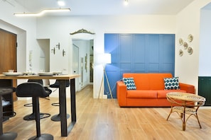 A modern living room with a blue accent wall, a dining area with a table and chairs, and a wicker side table. - Imma & Andrea Home - Your Stylish Salerno Retreat (Salerno)