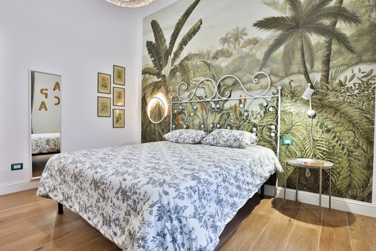 A bedroom with a bed, a wall mural, a mirror, and a bedside table.