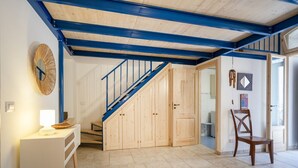 Een trap met blauwe leuningen, houten kastjes, een witte console tafel met een lamp en een houten stoel.