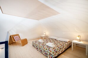 Un dormitorio acogedor en el ático, con una cama, una mesita, una silla y una lámpara.