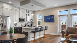 A modern kitchen with white cabinets, a stainless steel refrigerator, and a central island with bar stools. - Reluxme | Uptown 3BR w/ King Beds & Spa Access (Charlotte)