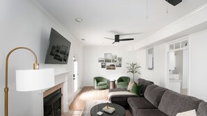 A modern living room with a fireplace, a large flat-screen TV, a ceiling fan, and a green sofa. - Family & Pet Friendly Modern Townhouse (Alabaster)