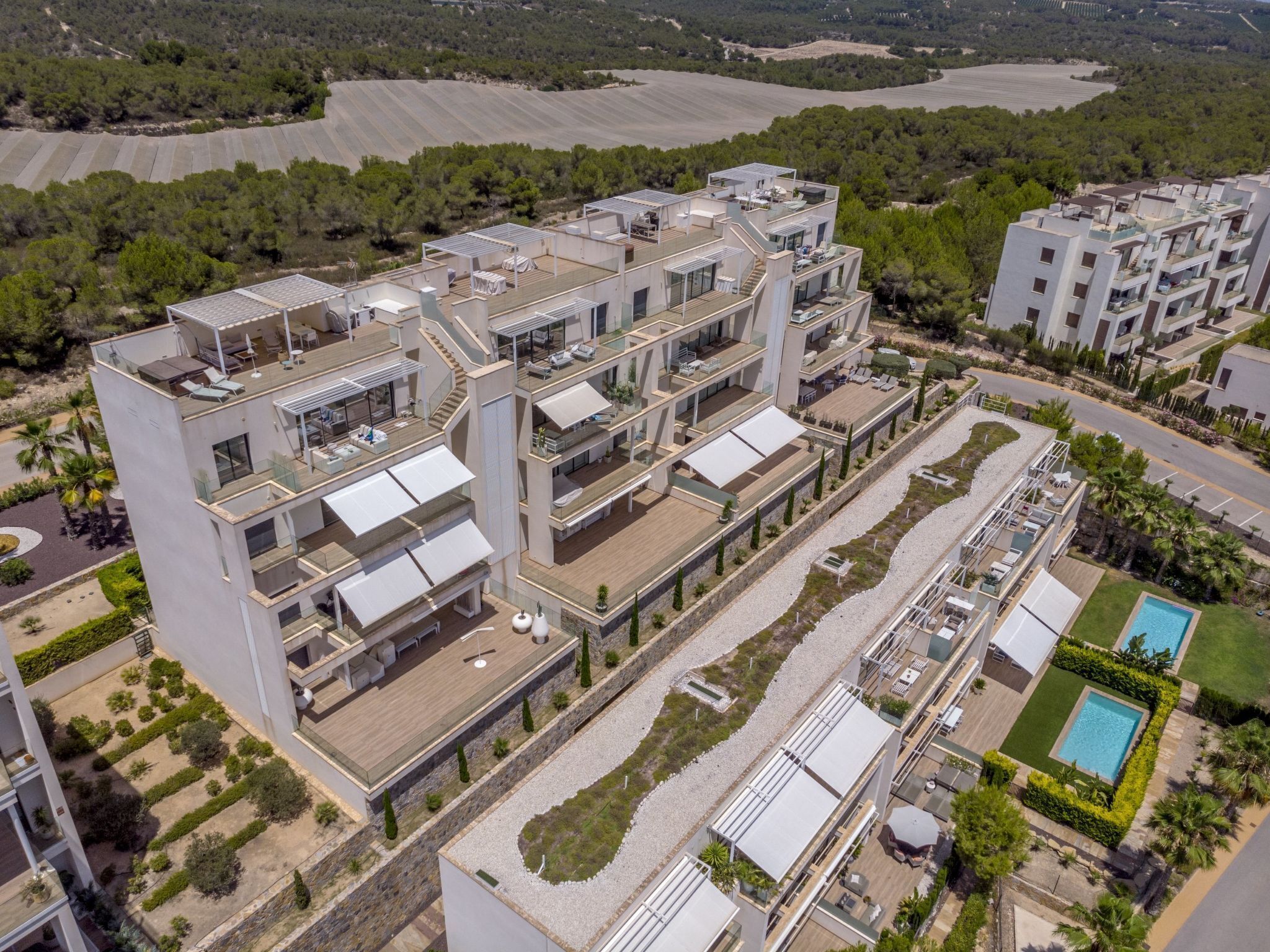 A modern multi-story residential building with rooftop terraces, a swimming pool, and landscaped gardens.