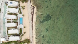 An aerial view of a beachfront hotel with multiple white buildings, a swimming pool, and a sandy beach.