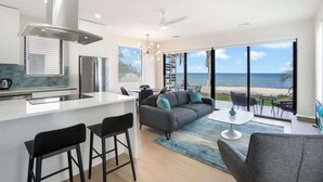 A modern kitchen with a large island, a dining area with a view of the ocean, and a living room with a sofa and chairs.