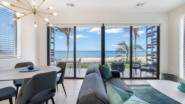 A modern living room with a large sliding glass door leading to a balcony overlooking a beach.