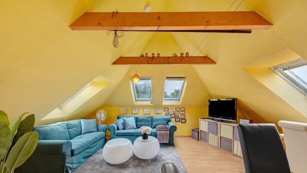 Uma sala de estar aconchegante com um sofá verde-água, dois pufes brancos redondos, uma cadeira preta e uma televisão em um armário de madeira.